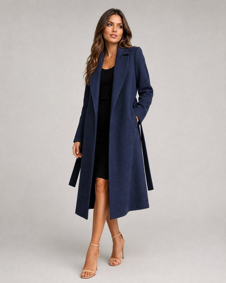 Navy belted long coat with lapel collar worn over a black mini dress
