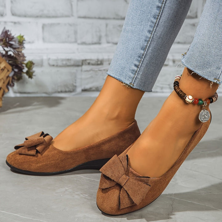 Black suede bow ballet flats worn on crossed feet with anklet