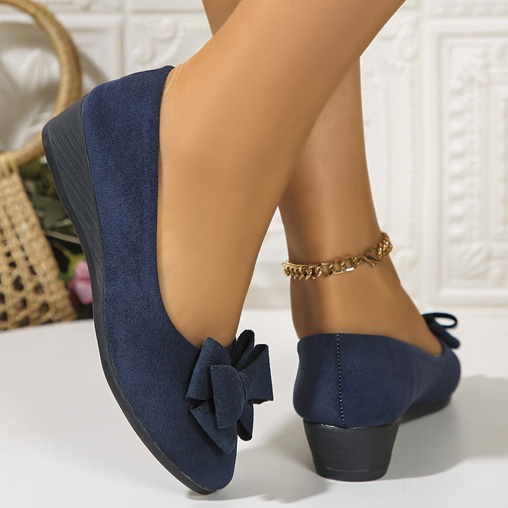 Navy suede bow ballet flats worn with crossed legs and gold anklet