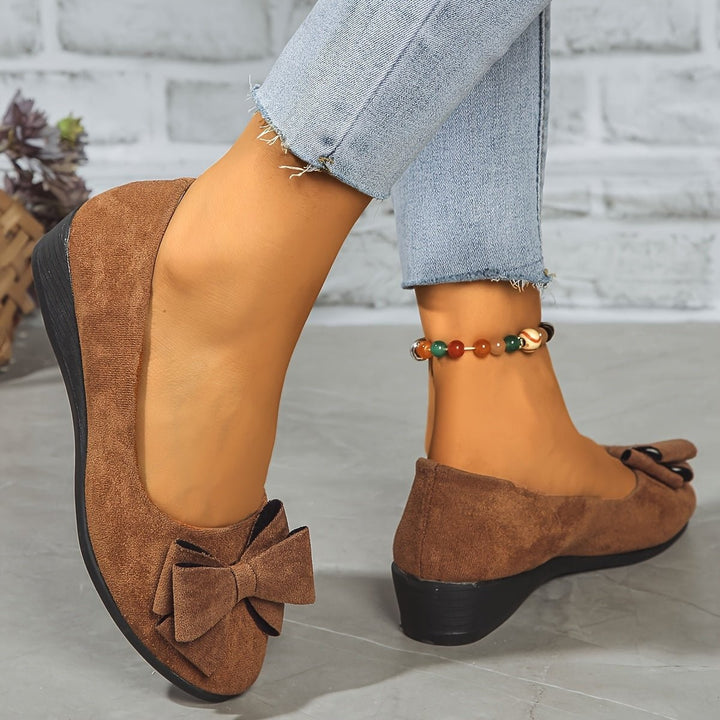 Black suede bow ballet flats paired with fringed denim clutch