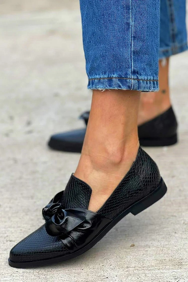 pointed-toe black loafer with glossy bow accent worn on foot