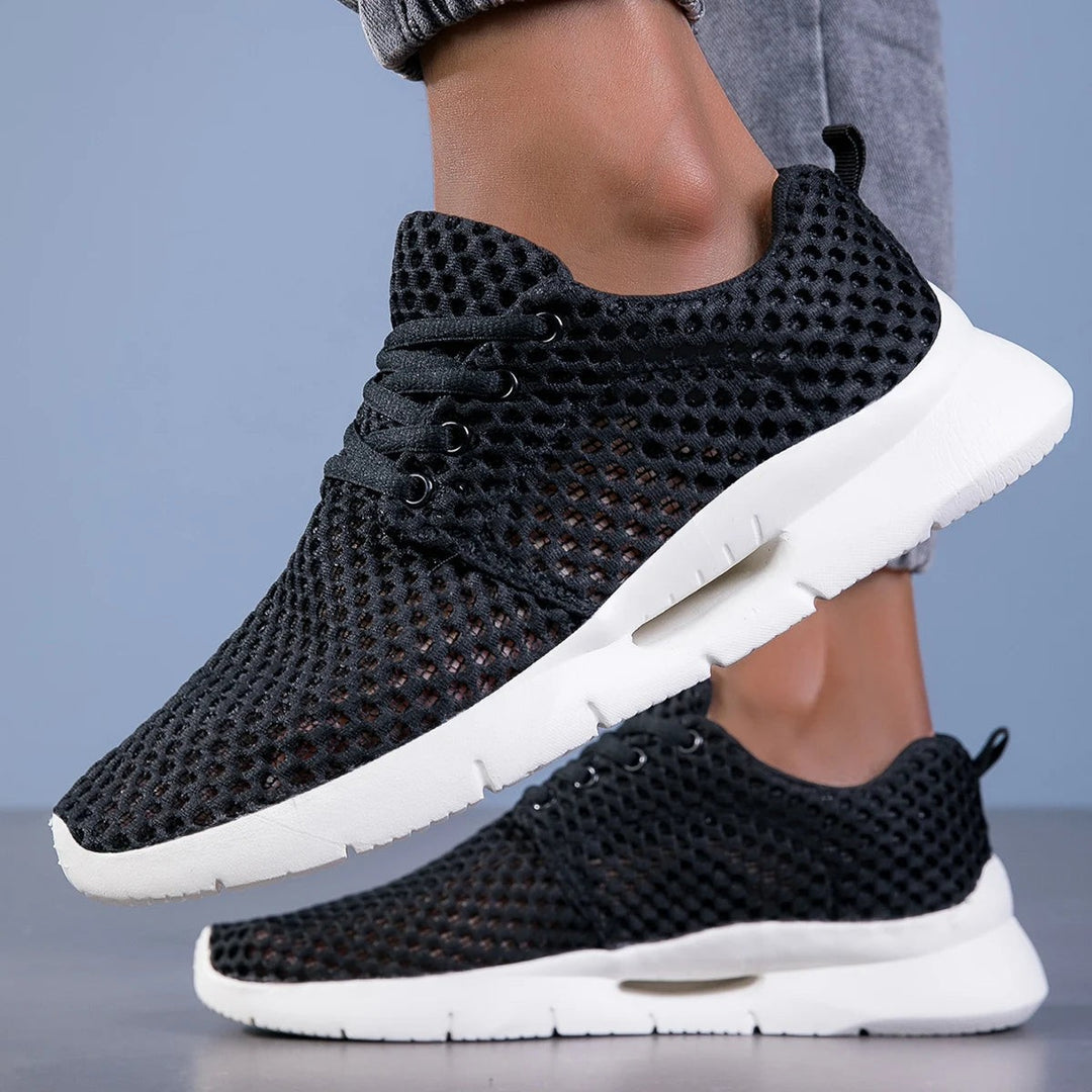 Black mesh sneakers with white sole and lace-up detail, worn on foot