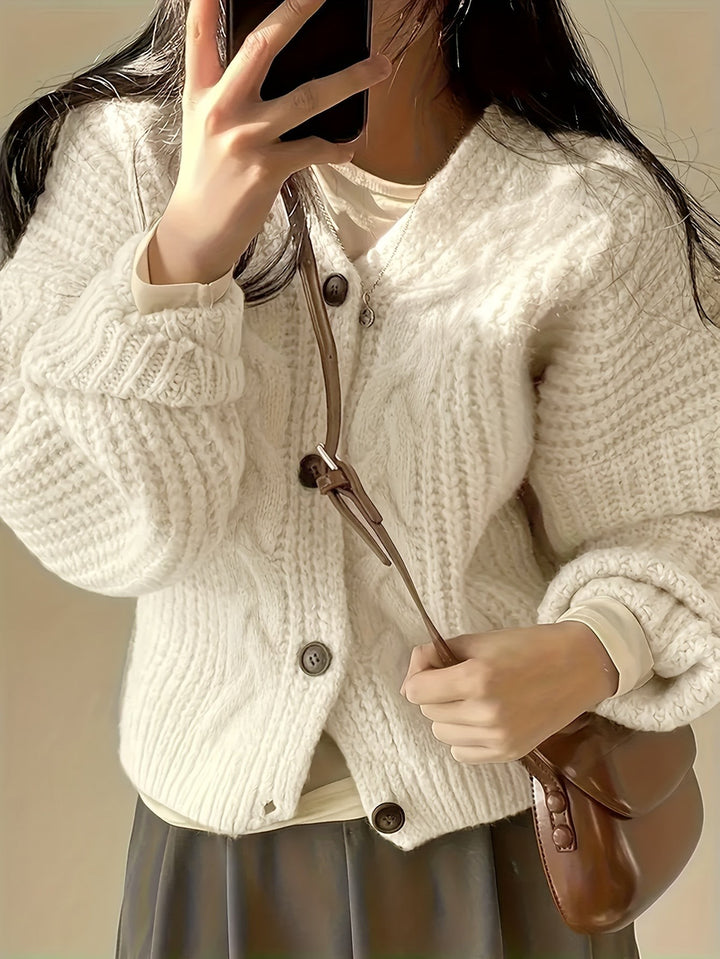 Close-up of ivory cable-knit cardigan buttons paired with brown leather bag strap