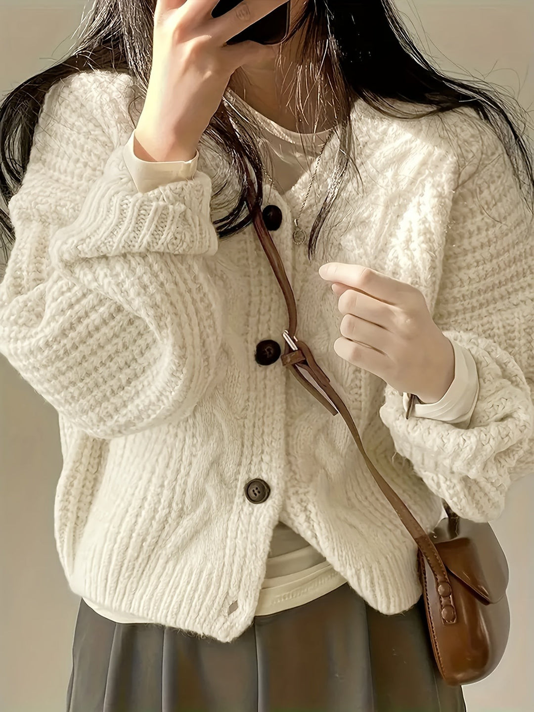 Oversized cream knit cardigan worn with pleated skirt and brown handbag