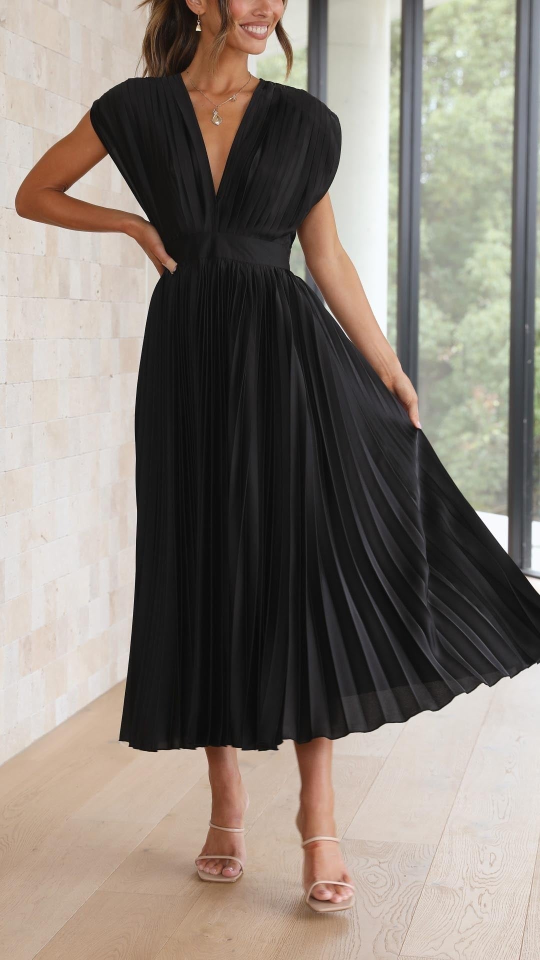 Smiling model in black pleated V-neck maxi dress with fitted waist