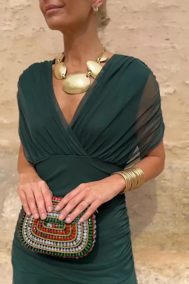 Close-up of emerald draped bodice with sheer sleeves and gold statement necklace