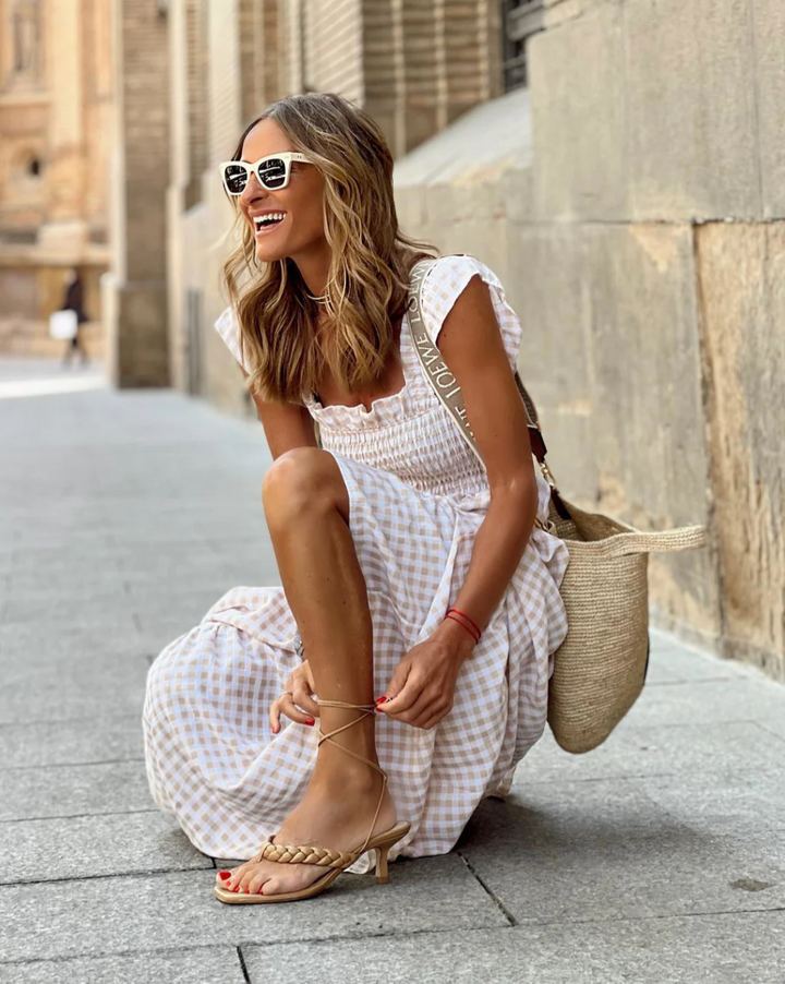 woman adjusting strappy sandal in beige gingham smocked maxi dress with ruffle straps