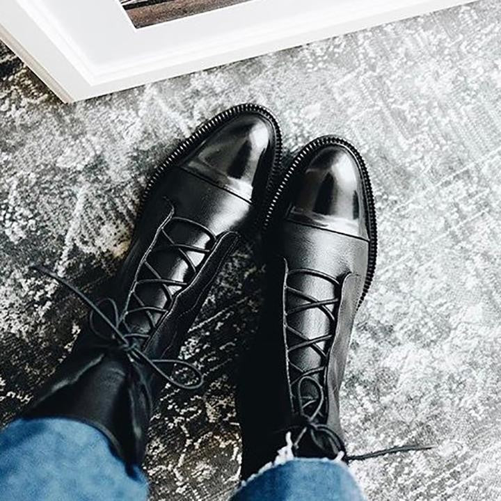Black leather cap-toe boots with crisscross laces on a patterned rug