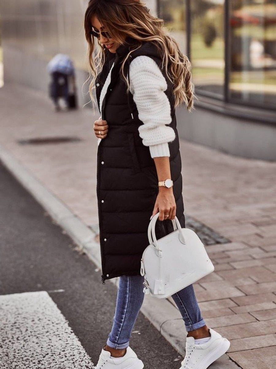 Woman in long black puffer vest paired with white sneakers and jeans