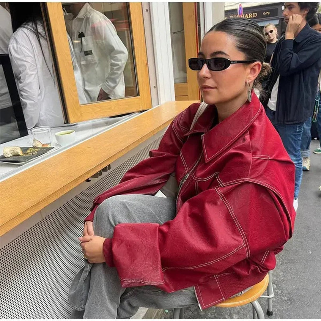 Oxblood oversized bomber jacket worn with gray sweatpants at a street cafe