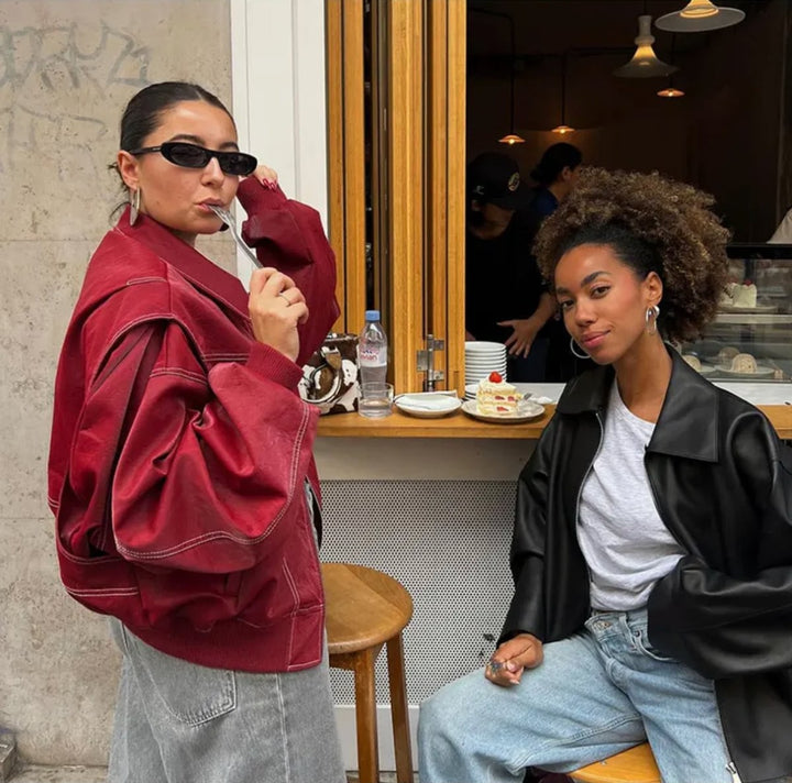 Woman wearing oversized red leather bomber jacket at an outdoor cafe table