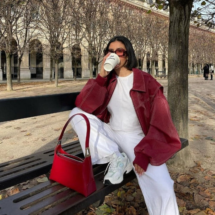 Red contrast-stitch bomber jacket layered over white outfit on park bench