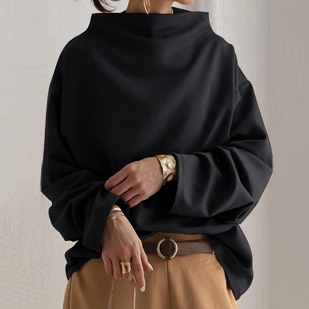 Black oversized mock-neck sweater with long batwing sleeves, worn over tan pants