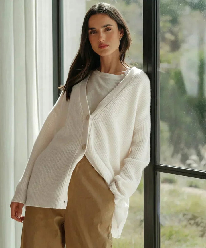 White ribbed cashmere cardigan draped over shoulders with tan trousers