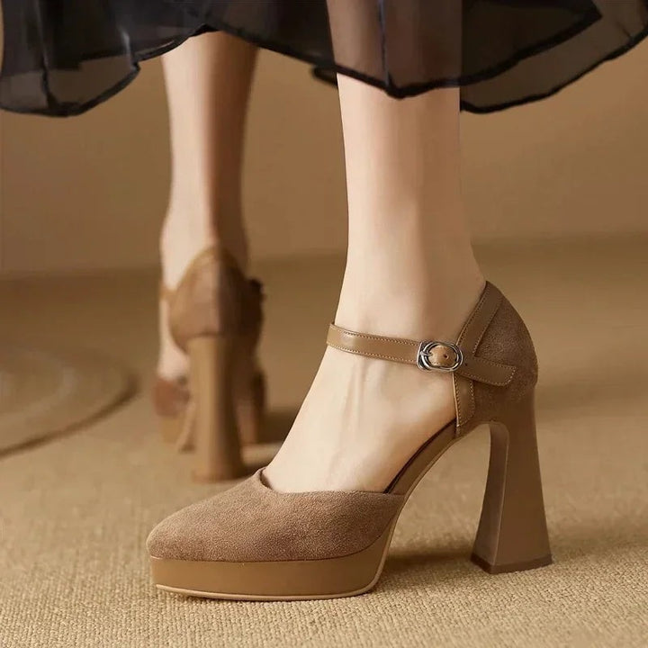 Tan suede pumps with leather ankle strap on carpeted floor