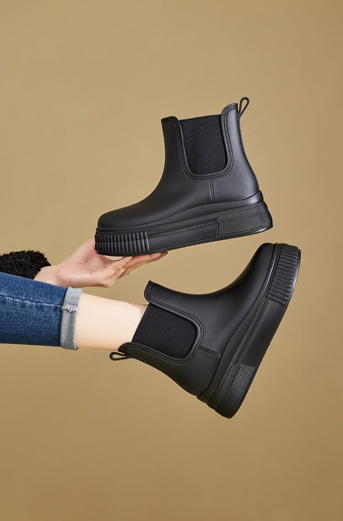 Black Chelsea rain boots held in hand showing thick ridged platform sole