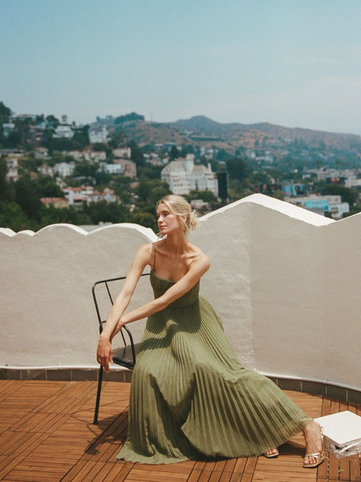 Woman seated in flowing olive green pleated maxi dress on rooftop terrace