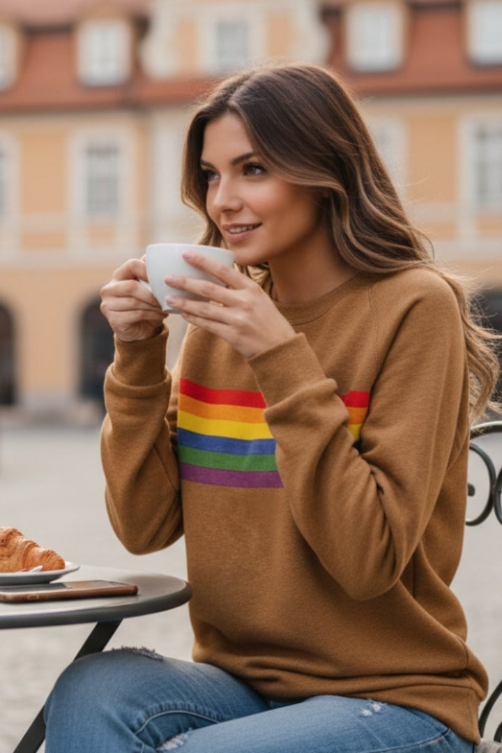 Camel pullover sweatshirt featuring rainbow stripe detail, styled with distressed denim jeans