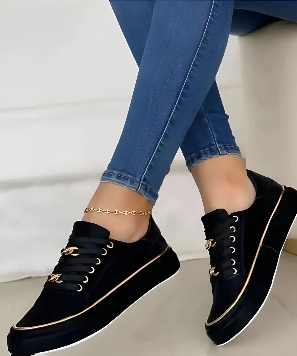 Black platform sneakers featuring gold piping and metallic chain accents