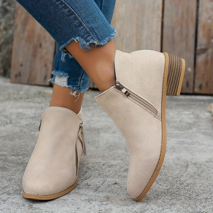 beige suede ankle bootie with metallic zip detail, worn on foot