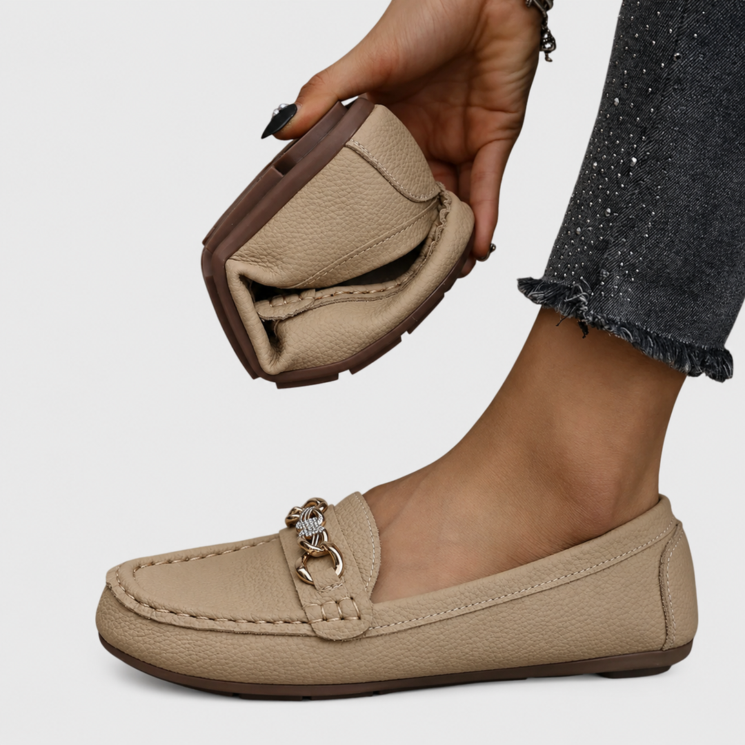 beige leather loafer flat held by hand showing flexible rubber sole