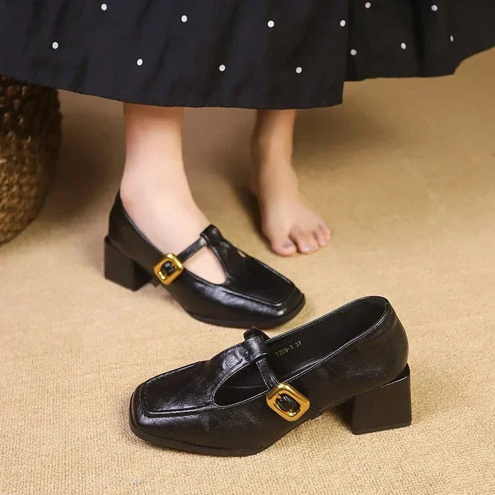 Black block heel Mary Janes with T-strap and gold buckle, worn on feet