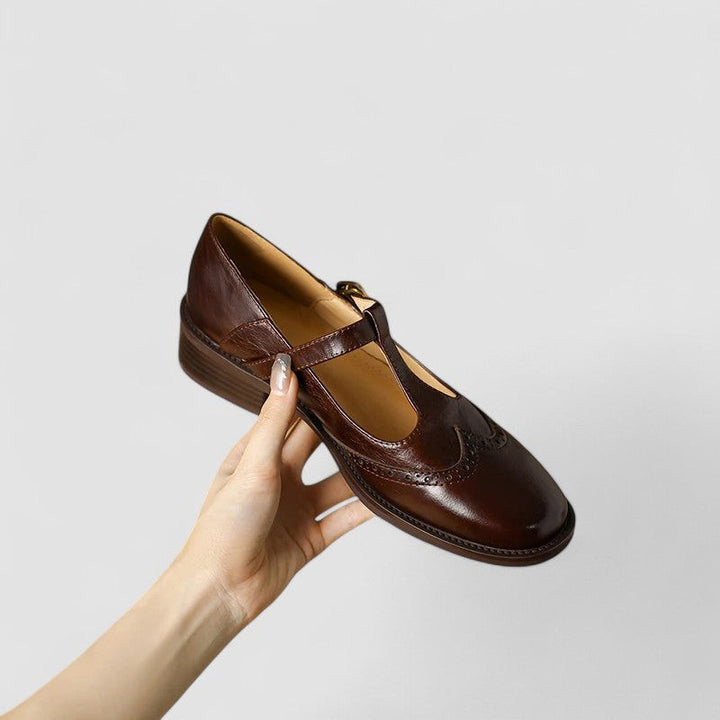 brown leather Mary Jane shoe held by hand showing T-strap buckle design