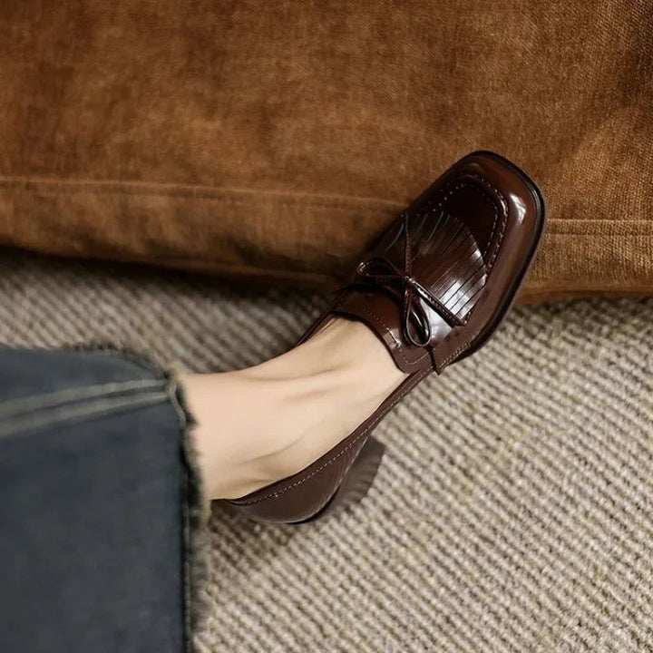 brown patent leather tassel loafer pump peeking from denim skirt hem