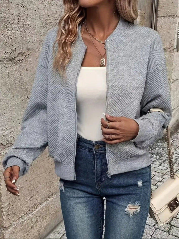 Gray textured zip-up bomber jacket paired with ripped denim jeans