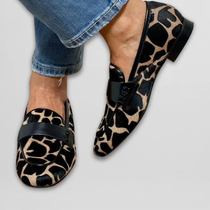 Close-up of giraffe-print flat loafers featuring black leather trim and low stacked heel