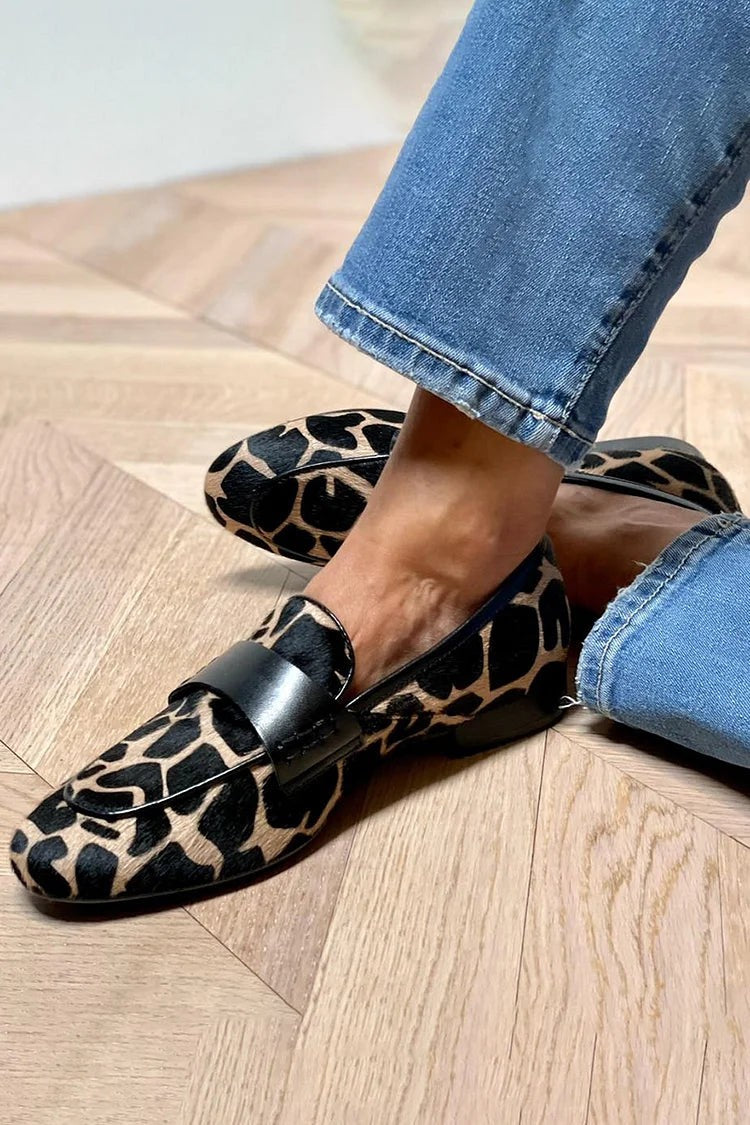 Animal-print flat loafers with black leather panel styled on herringbone wood flooring