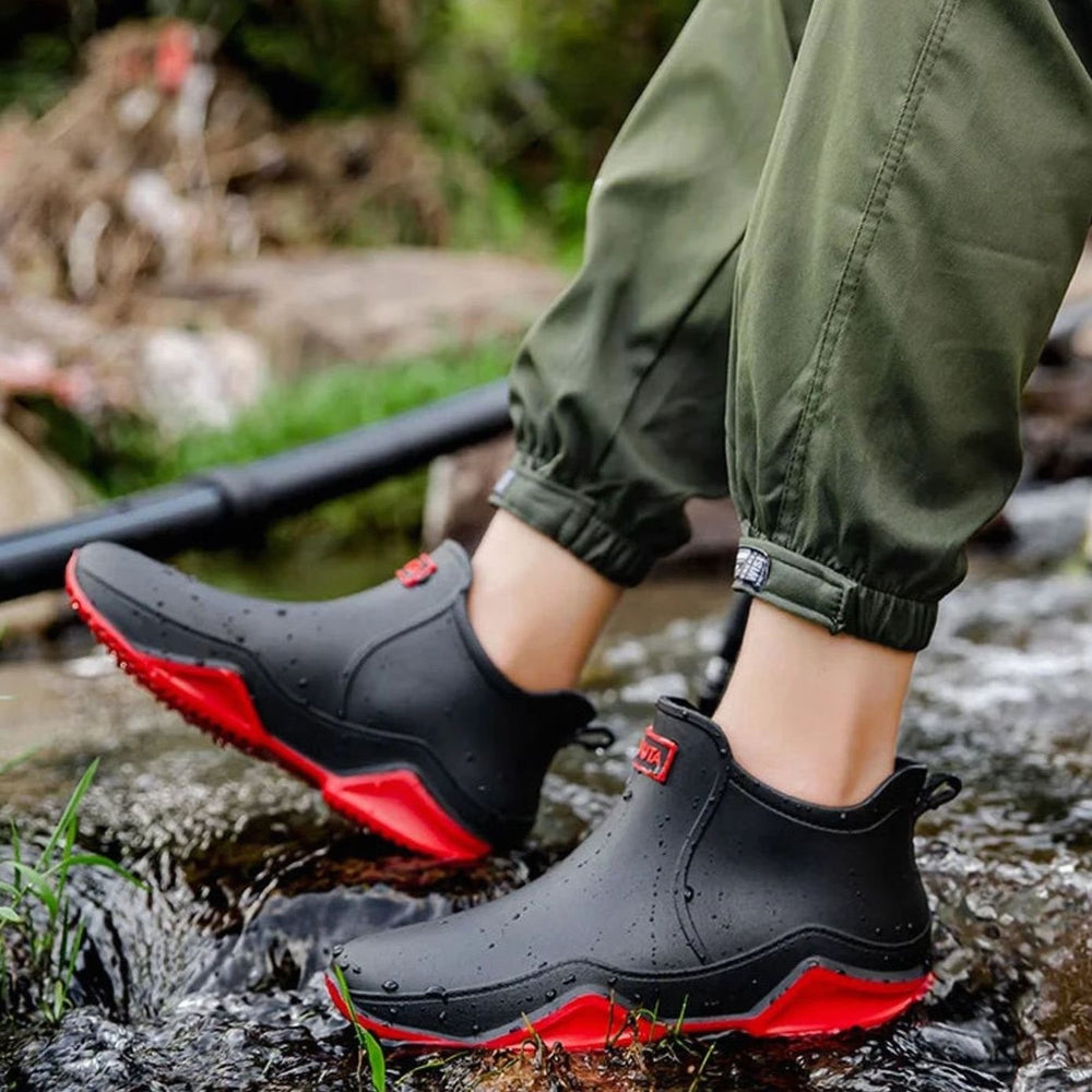 black slip-on rain boots with red sole worn while stepping through creek
